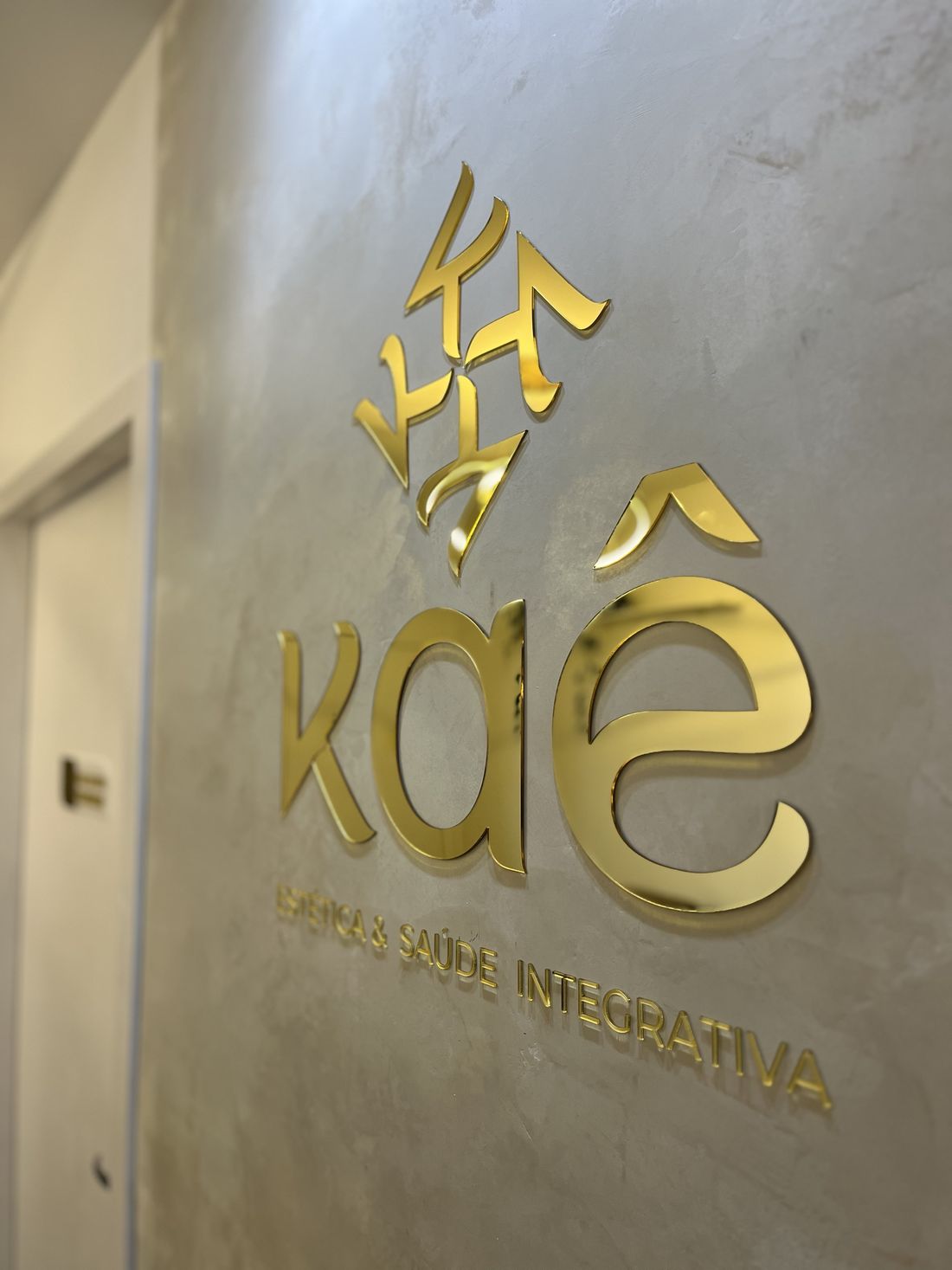 Logotipo da Kaê em dourado na parede da recepção da clínica.